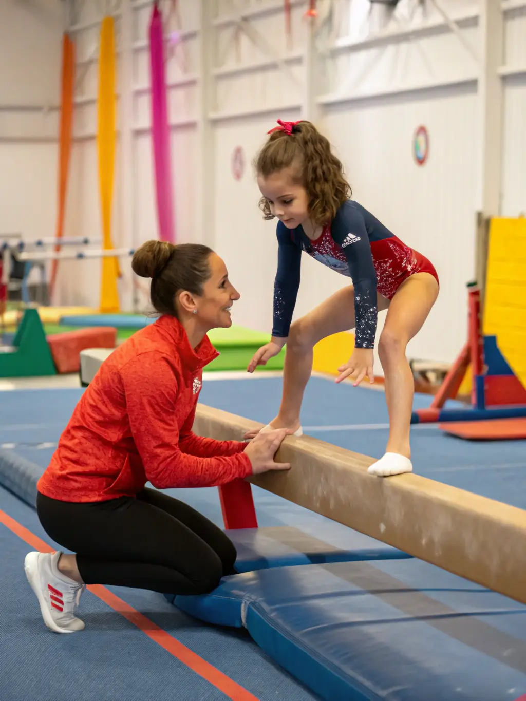 A photo of a gymnastics instructor spotting a young gymnast as they practice a handstand on a balance beam, showcasing expert guidance and safety.
